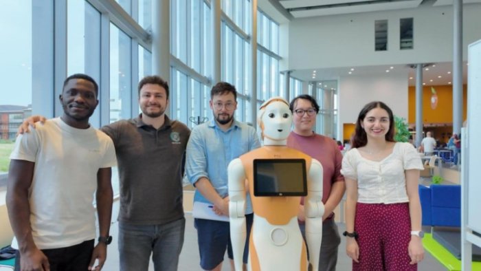 Team of people standing behind a humanoid robot