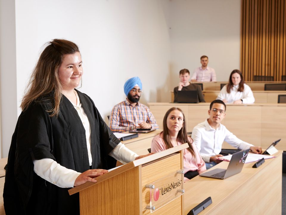 A smiling student standing at a podium of a modern courtroom