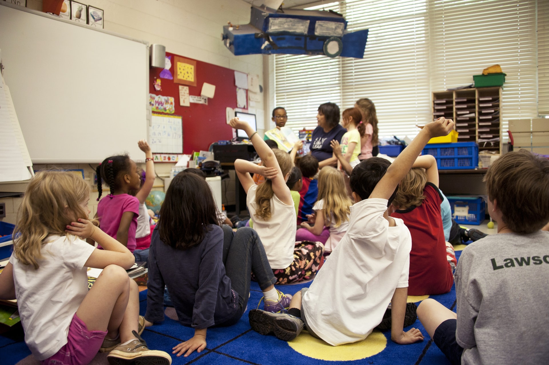 Teacher reading to young children at school. Children sat on the floor facing the teacher who is holding the book for them to see. 