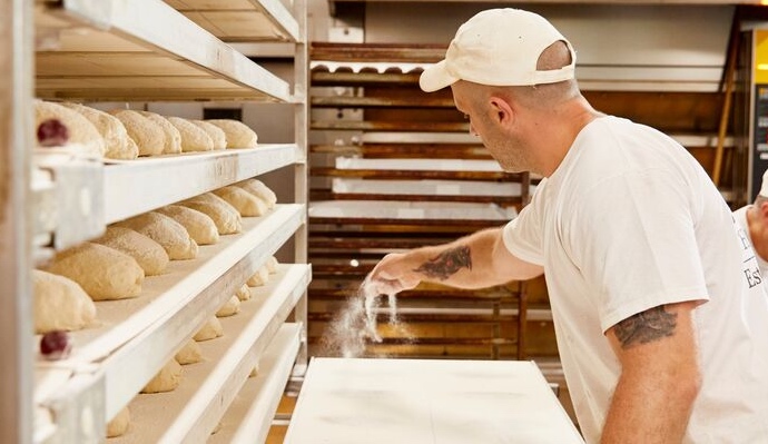 Baker working in a bakery spreading some flour onto a work surface