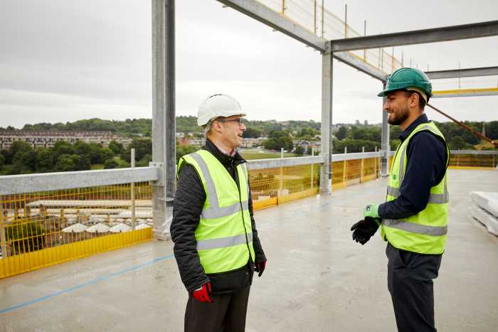 Image shows Declan Fahy, Hallam Alliance Programme Coordinator and Toby Ward, Head of Estates and Workplace Development. Both are wearing hi viz jackets and helmets and are on top of one of the new buildings on Howard Street
