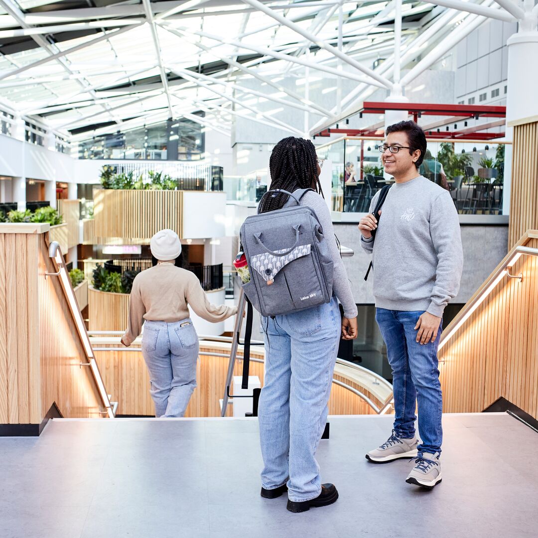 Image shows two students in the atrium, talking. One student is walking down the stairs. The atrium is bright and airy thanks to the new renovations.