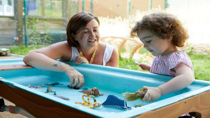 An early years practioner and toddler playing in a water tray