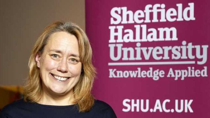 Image shows Vice Chancellor of Sheffield Hallam University, Liz Mossop. She is standing in front of a pink banner stand that says "Sheffield Hallam University. Knowledge Applied. Shu.ac.uk"