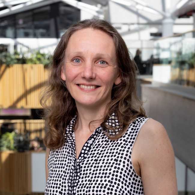 Image shows Libby Wilson, Chief Operating Officer, smiling at the camera. She is standing in the Owen Building atrium. 