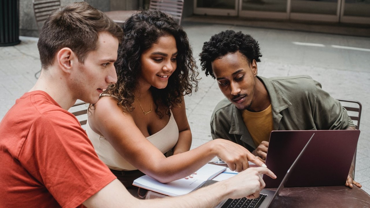 Image shows three students around a laptop working together