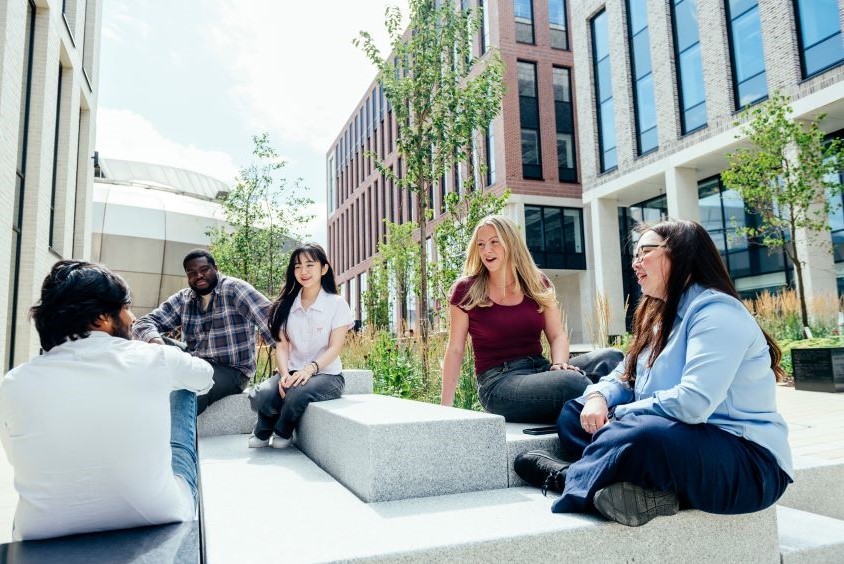 Image shows five students sitting on Hallam Green, socialising.