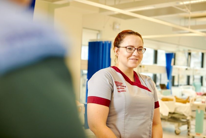 Image shows a female nurse wearing Sheffield Hallam University uniform. She is on a hospital ward and is looking away from the camera.