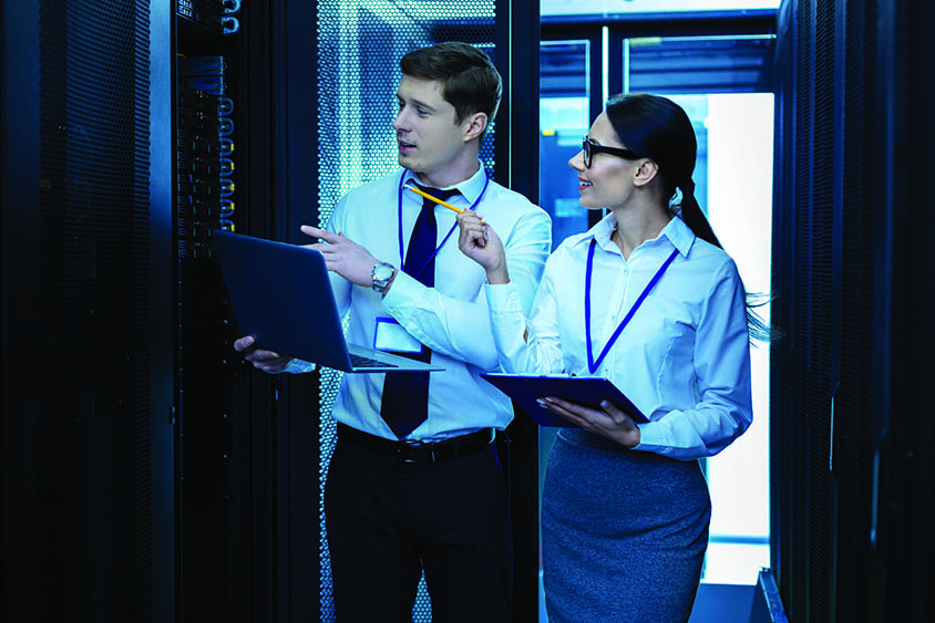 Two students with laptops looking at a server rack