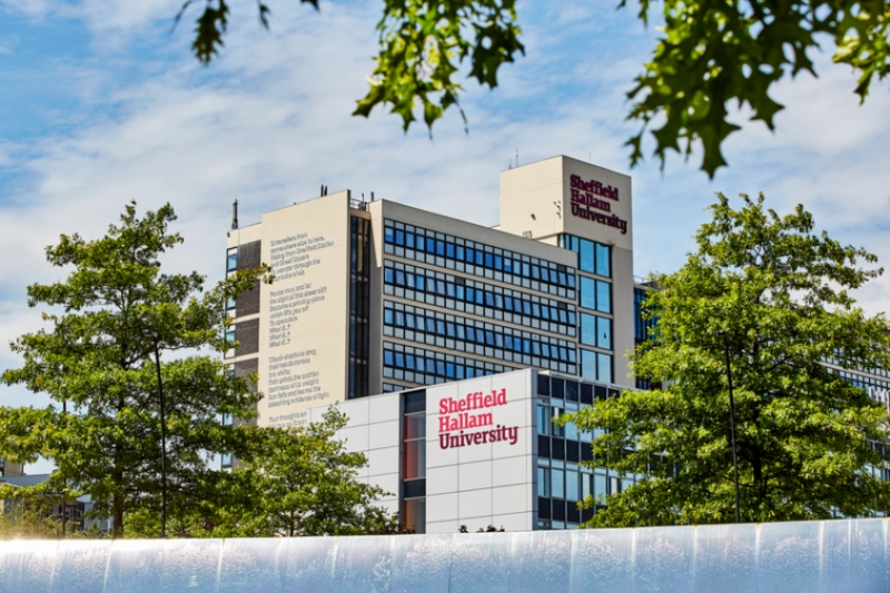 Image of Sheffield Hallam University against a blue sky and surrounded by trees