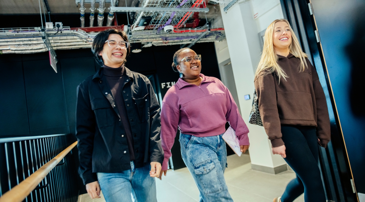 Three students walking down the business school corridor.