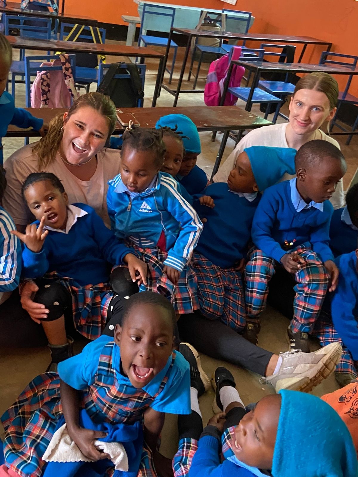 Children and two adults sitting on the floor of the classroom