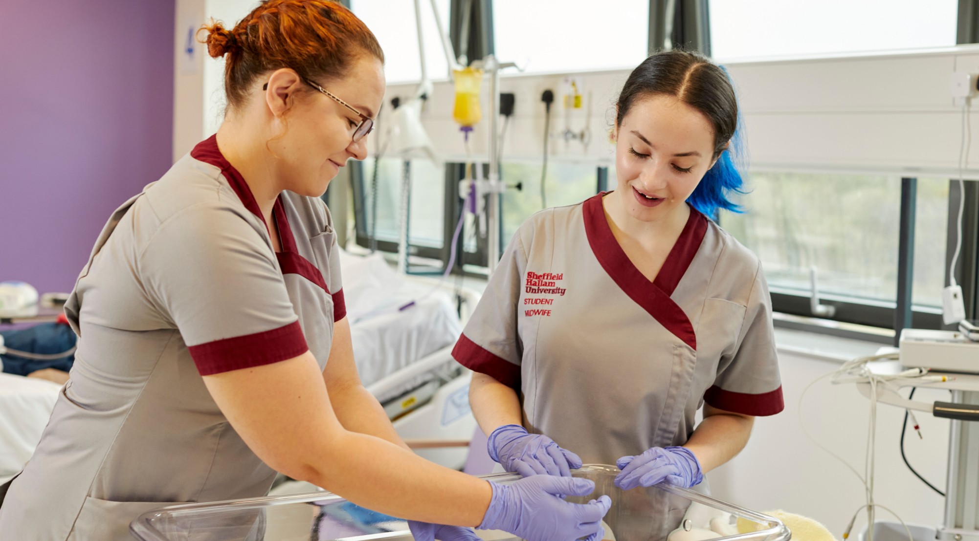 Two students in uniform looking after a baby in a maternity ward.