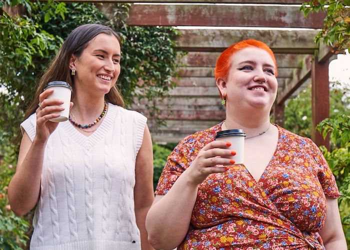 Two female students walking and carrying coffee cups