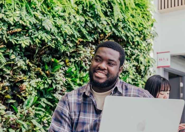 A male student smiling while using a laptop in a Sheffield Hallam study space