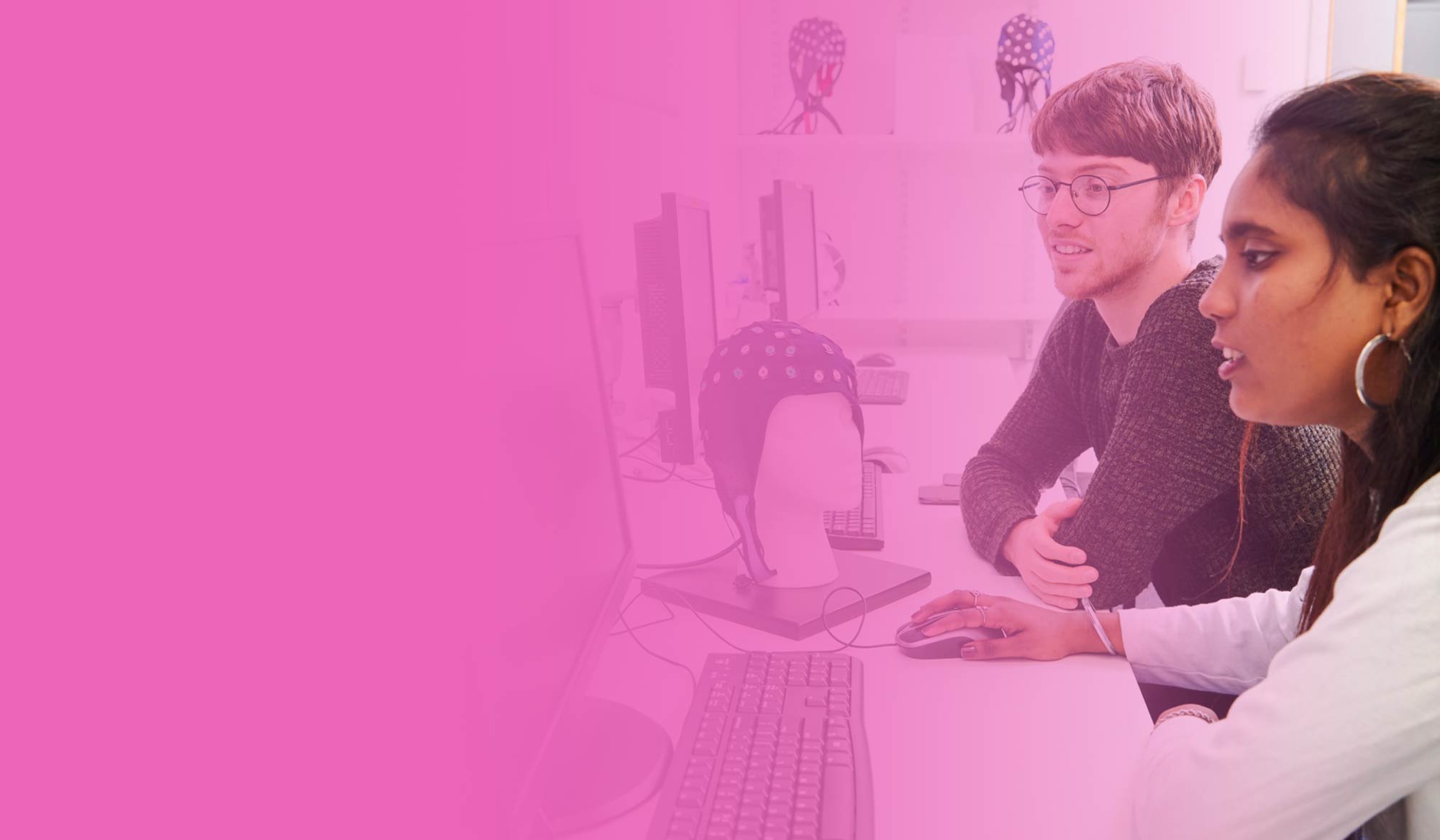 Students working at a PC in a lab, against a pink gradient background