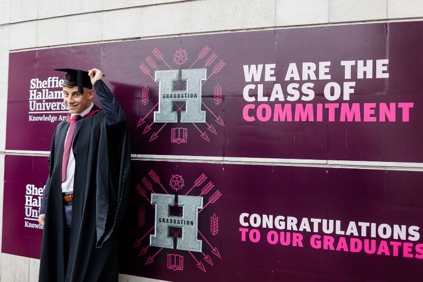 A graduate standing in front of celebratory graduation visuals  