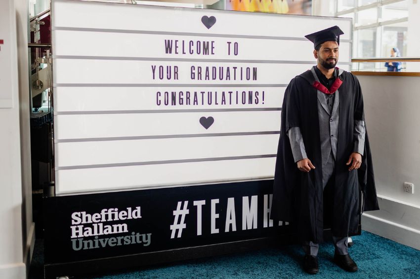 A student graduating standing in front of a lightbox having a photo taken