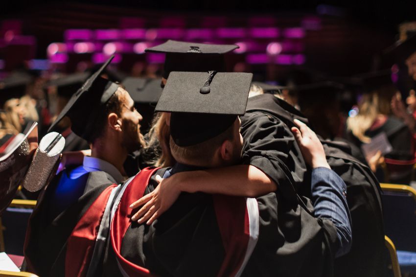 Students hugging at ceremony wearing graduation gowns
