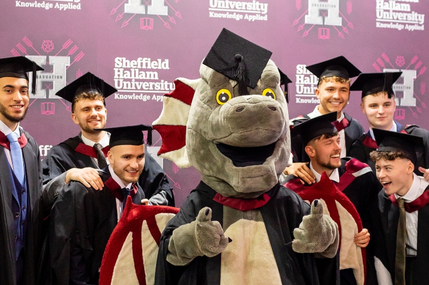 A dragon mascot posing with a group of graduates