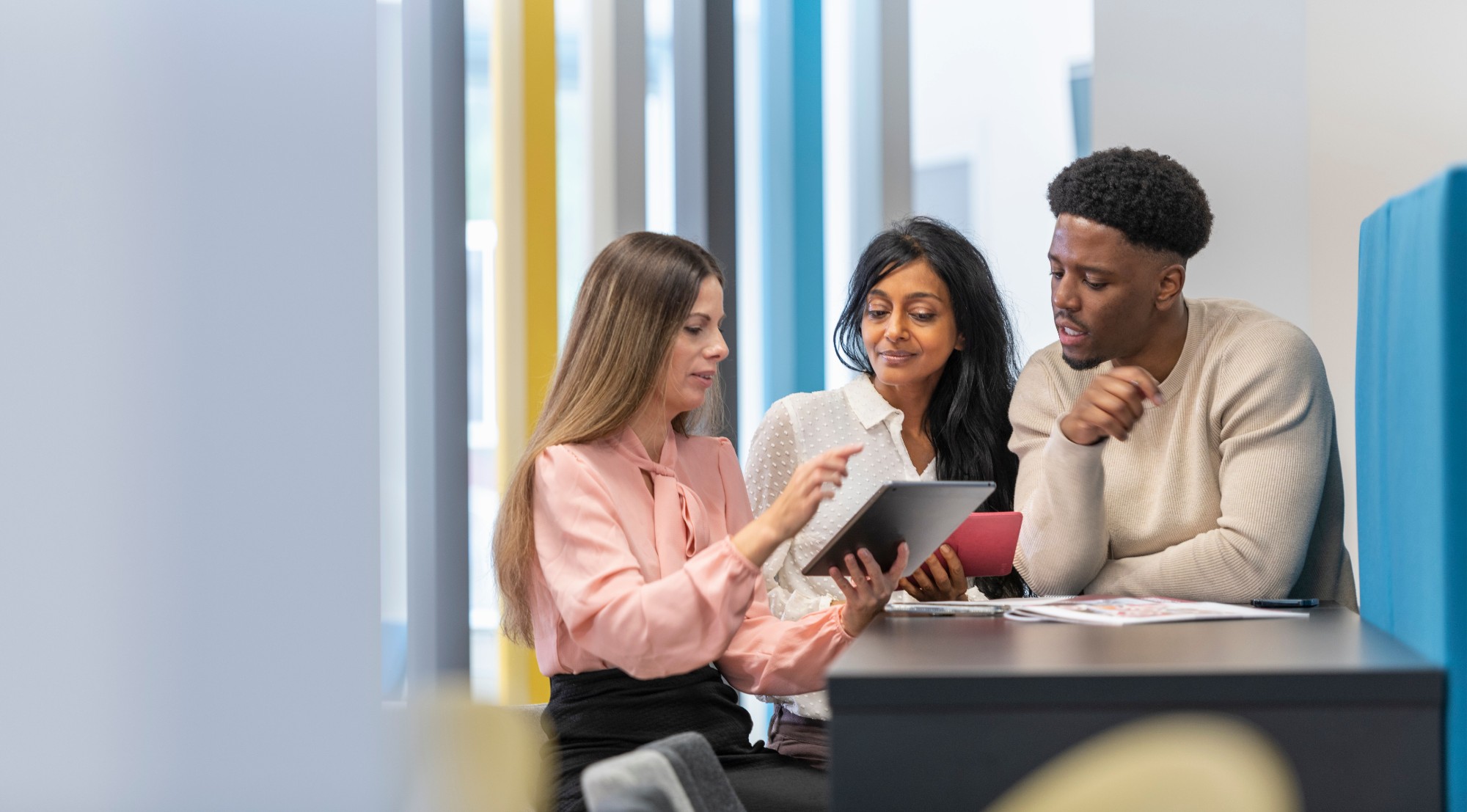 Three students in a corporate office setting looking at a piece of academic written work