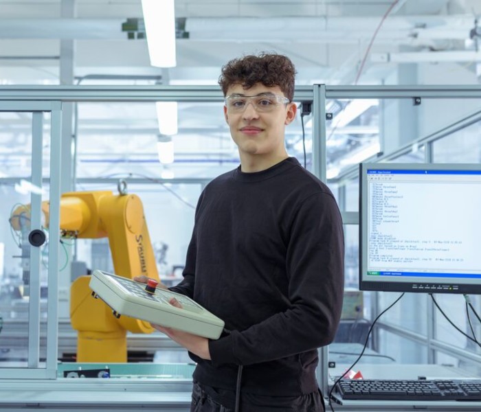 A student operating industrial robotics equipment in an engineering lab.