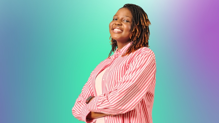 A smiling student in a pin stripe shirt standing with arms crossed against a colourful gradient background.