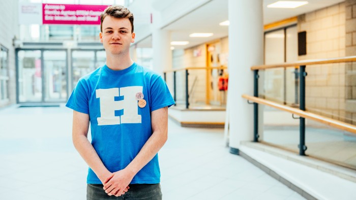An open day ambassador stood in the Sheffield Hallam atrium wearing a blue Team Hallam t-shirt.