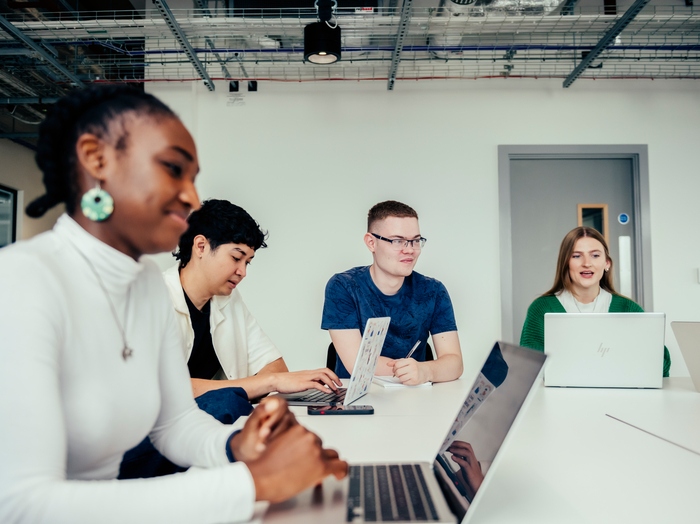 Group of four students sat around a table, looking at laptops