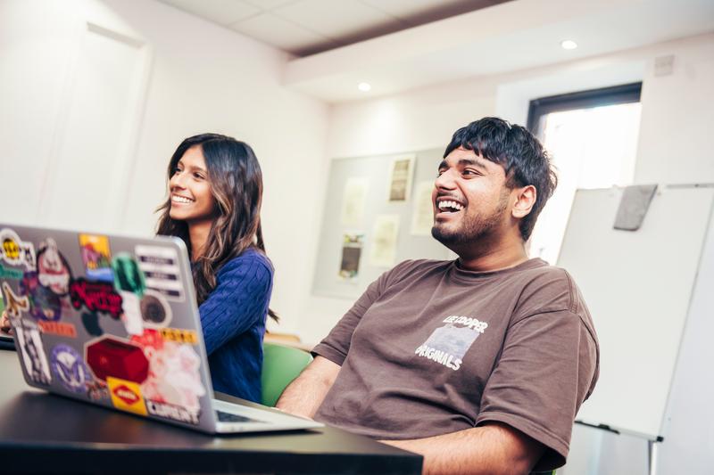 Two students smiling behind a laptop