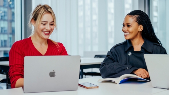 Two students with laptops, laughing together