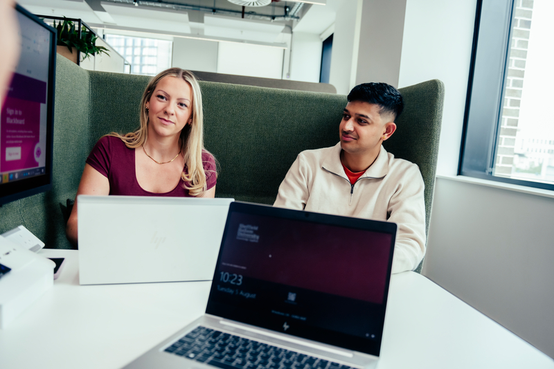 Two students smiling behind a laptop
