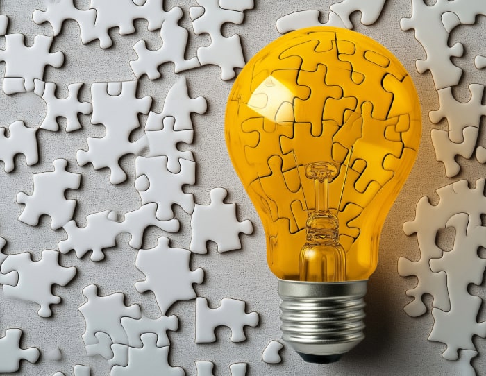 A yellow glass lightbulb sits on top of jigsaw pieces. Some pieces are viewed through the glass, creating a distortion.