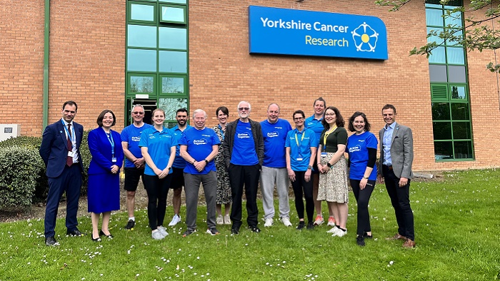 Group of men and women stood on grass outside building with Yorkshire Cancer Research logo on it 