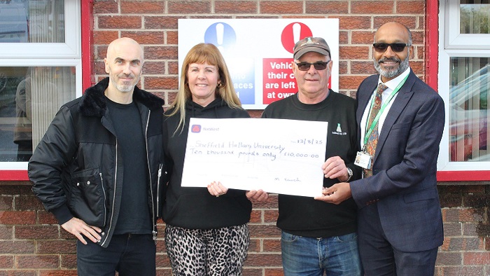 Four people stood outside a brick building holding a large cheque