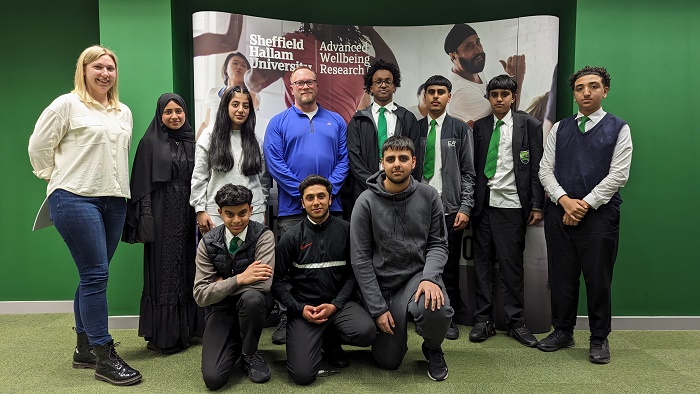 Charlotte Jackson and Dave Hembrough with young people from Darnall stood in front of a banner at the Advanced Wellbeing Research Centre