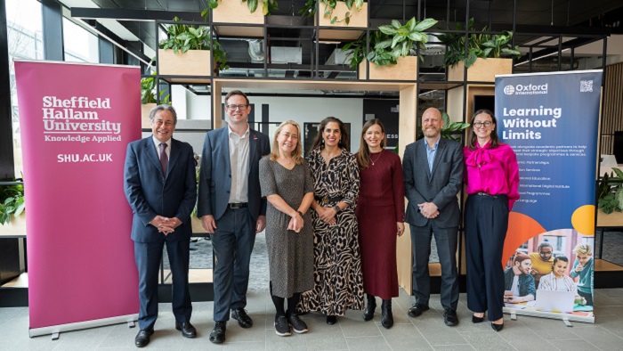 Group of seven people stood smiling to camera in front of two banners 