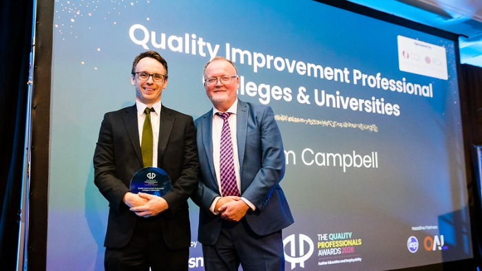 Colm Campbell stood holding the award in front of a screen which says 'Quality improvement professional colleges and universities'.