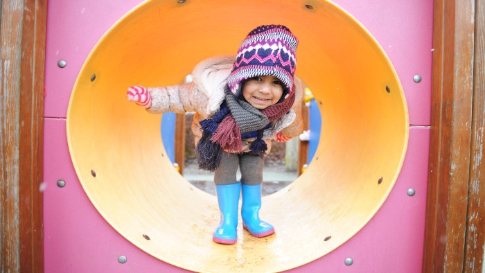 A young child in a yellow plastic playground tunnel, smiling at the camera