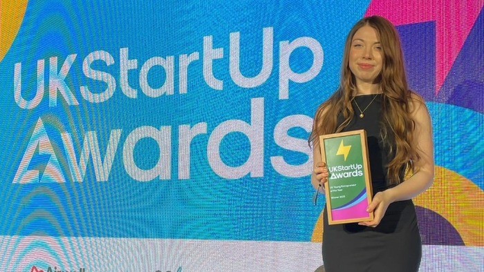 Emma Redfern holding the Young Entrepreneur of the Year award, stood in front of a backdrop that says UK Start Up Awards.