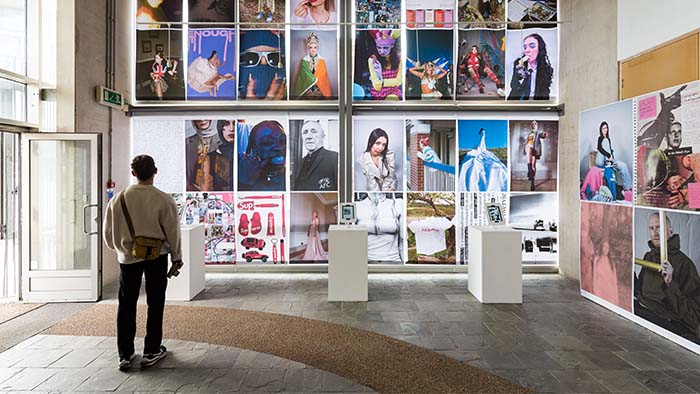 An exhibition at Sheffield Hallam University with various artworks displayed on the walls. A person is pictured from behind observing the artwork. 