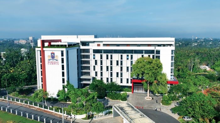 An aerial image of a large white university buildings surrounded by trees and greenery