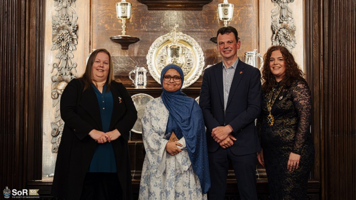 Four people stood in a wood panelled room with lights behind them