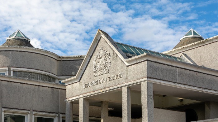 Exterior of a court building in the UK, a grey concrete building with 'courts of justice' on the front. 