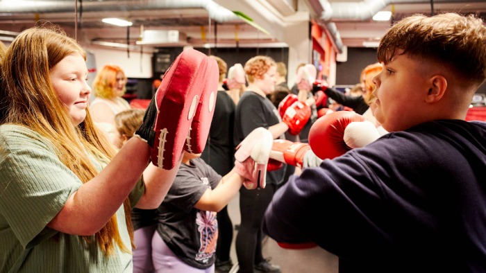 Two young people, a girl holding boxing pads on the left and a boy using boxing gloves on the right, practising boxing drills at a CEW workshop.