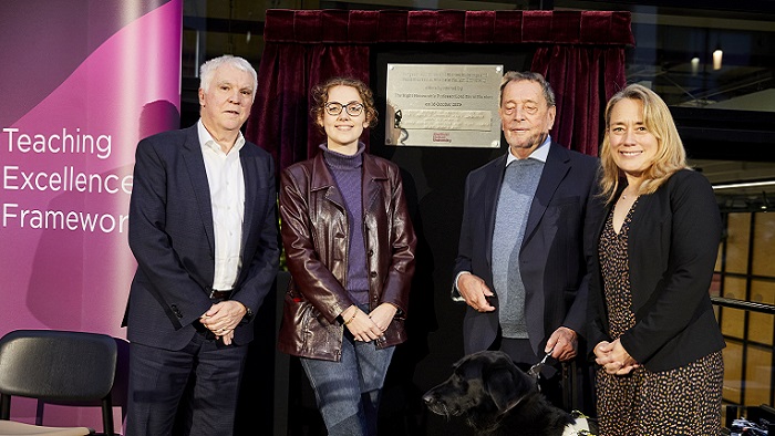Four people smiling towards the camera stood in front of a plaque 