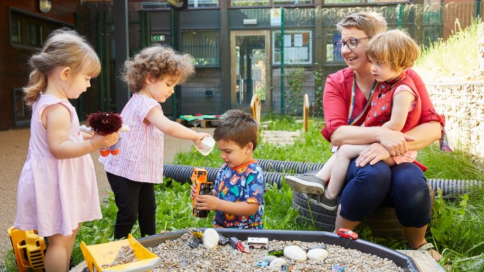 Nursery worker playing outside with four young children