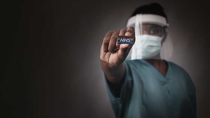 Nurse in mask and visor holding out NHS rainbow badge
