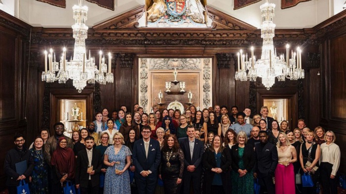 Large group of people stood in a wood panelled room with two big chandeliers