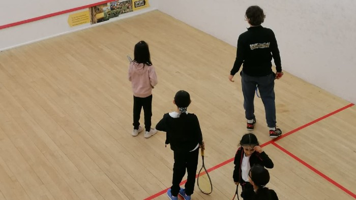 Young children playing squash on an indoor squash court